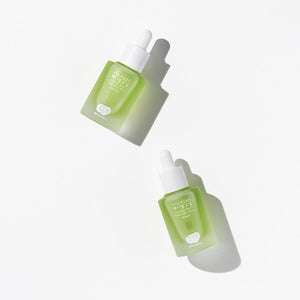 Whamisa ﻿Organic Flowers Facial Oil Refresh bottled in a semi-transparent bottle with lime green content inside. The cap works as a dropper. Two bottles are arranged on a white background.